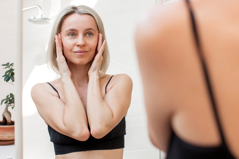 A woman looking in the mirror considering a brow lift in Suffolk County